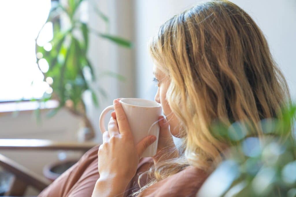 Woman sitting with a mug of tea, taking a mindful pause to reflect during a values conflict and reconnect with what matters most.