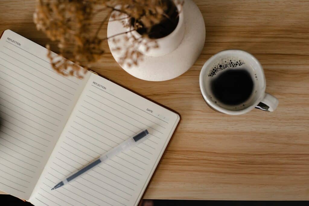 A notebook and cup of coffee on a table symbolising a quiet moment for reflection and planning to create balance in life