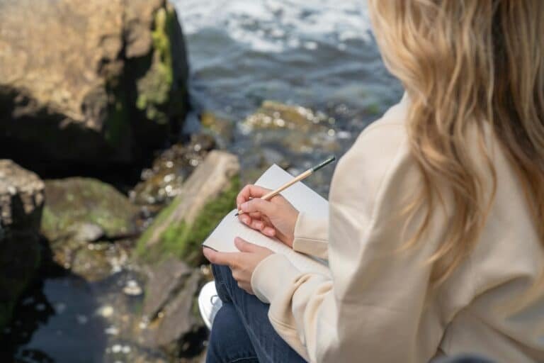 Woman journaling outdoors with a notebook, representing taking a quiet moment to balance your life through reflection