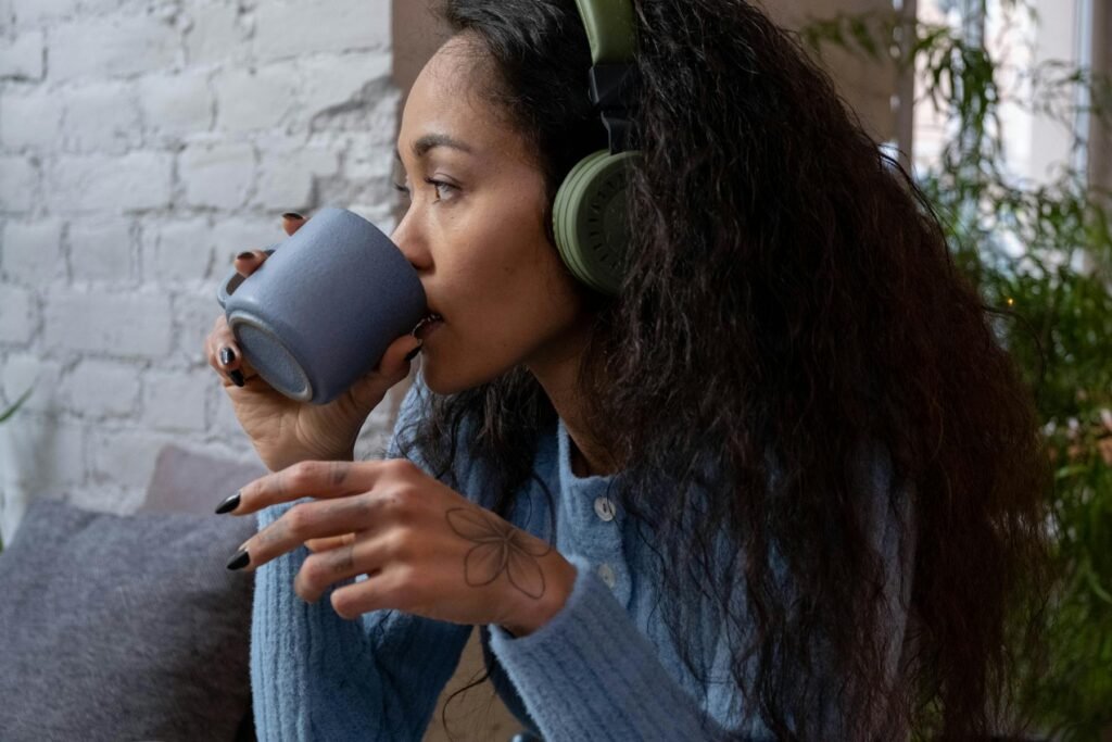 Woman wearing headphones drinking a coffee - demonstrating listening to music or a podcast is one of the hobbies for relaxation women can do after a busy day