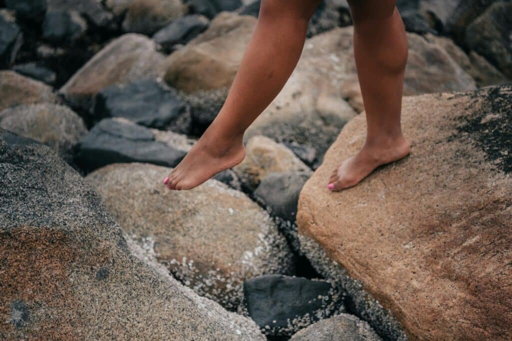A woman walking barefoot on stepping stones – representing navigating new territory when trying to be true to yourself and live authentically