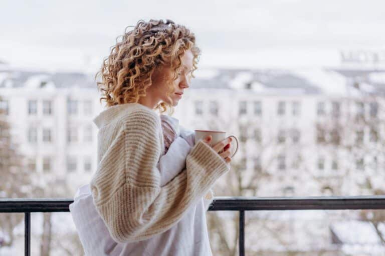 Woman stood on balcony, looking thoughtful with cup of tea, wondering how to be true to yourself and live authentically when others don't understand
