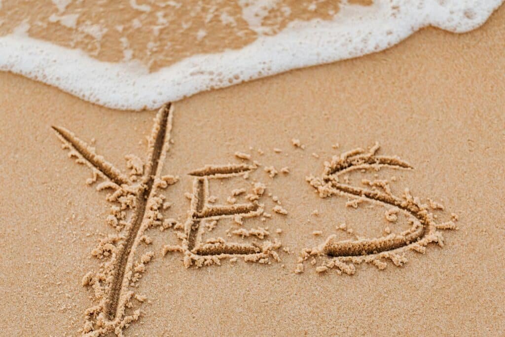Yes written in the sand, about to washed away by a wave, symbolising letting go of saying yes to everything 